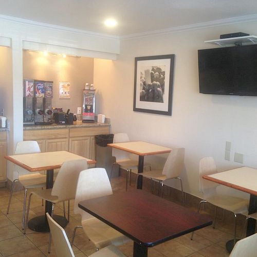 This image shows a small dining area with several tables and chairs, a television mounted on the wall, and a beverage station in the background.