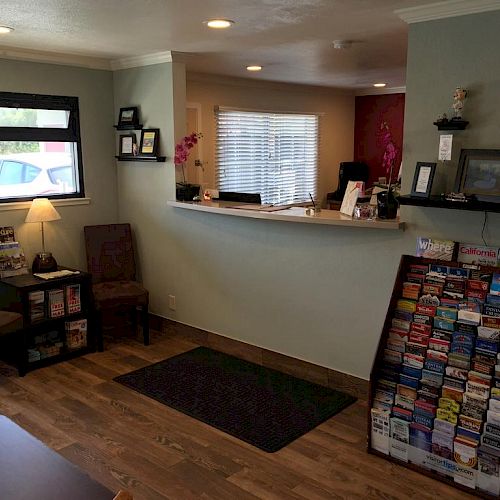 A cozy reception area with chairs, a front desk, a lamp, framed pictures, brochures on a display stand, and a window with blinds ends the sentence.