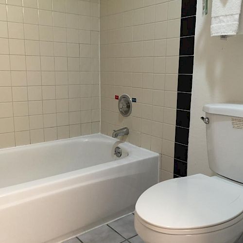 The image shows a bathroom with a white toilet, a bathtub with a shower curtain, tiled walls, and a towel hanging on a rack.