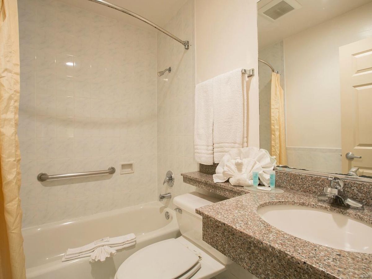 A clean bathroom with a bathtub, shower curtain, toilet, sink, granite countertop, towels, and decorative towel origami on the counter.