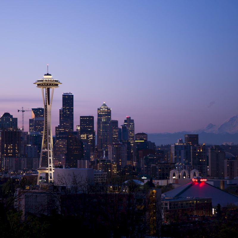 Cityscape photo of Seattle with the Space Needle prominently featured, skyscrapers in the background, and Mount Rainier visible on the horizon.