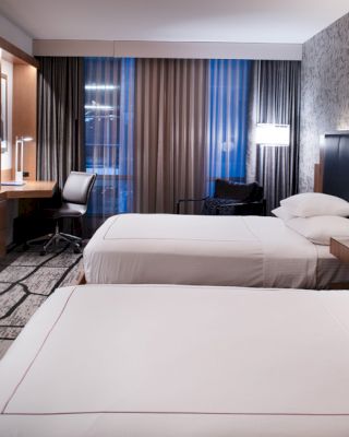 A modern hotel room with two beds, a flat-screen TV, a desk with a chair, and stylish decor, including patterned wallpaper.
