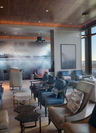 A modern lounge with comfortable seating, cityscape mural, and large windows offering a scenic waterfront view with a Ferris wheel outside.