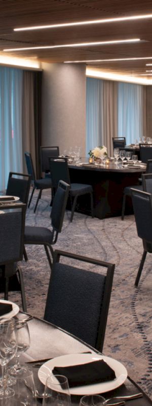 A banquet hall is set up with round tables, each adorned with place settings and floral centerpieces, under modern ceiling lights.