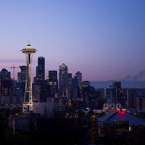 A skyline view of Seattle at dusk, featuring the Space Needle, surrounding buildings, and Mount Rainier in the background.